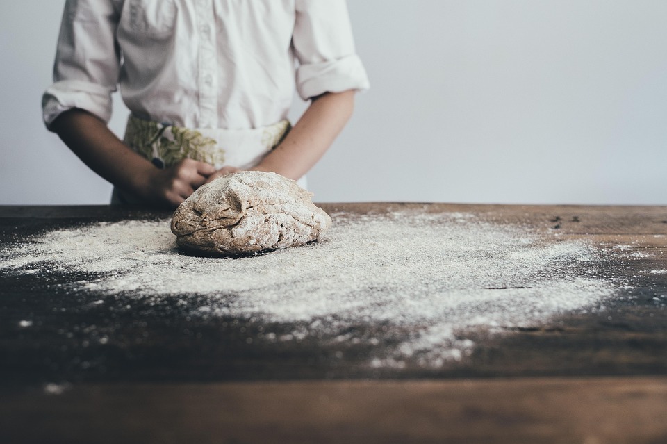Artisan baker shaping fresh bread dough on a floured wooden table at Crookies Bakery in Countesthorpe